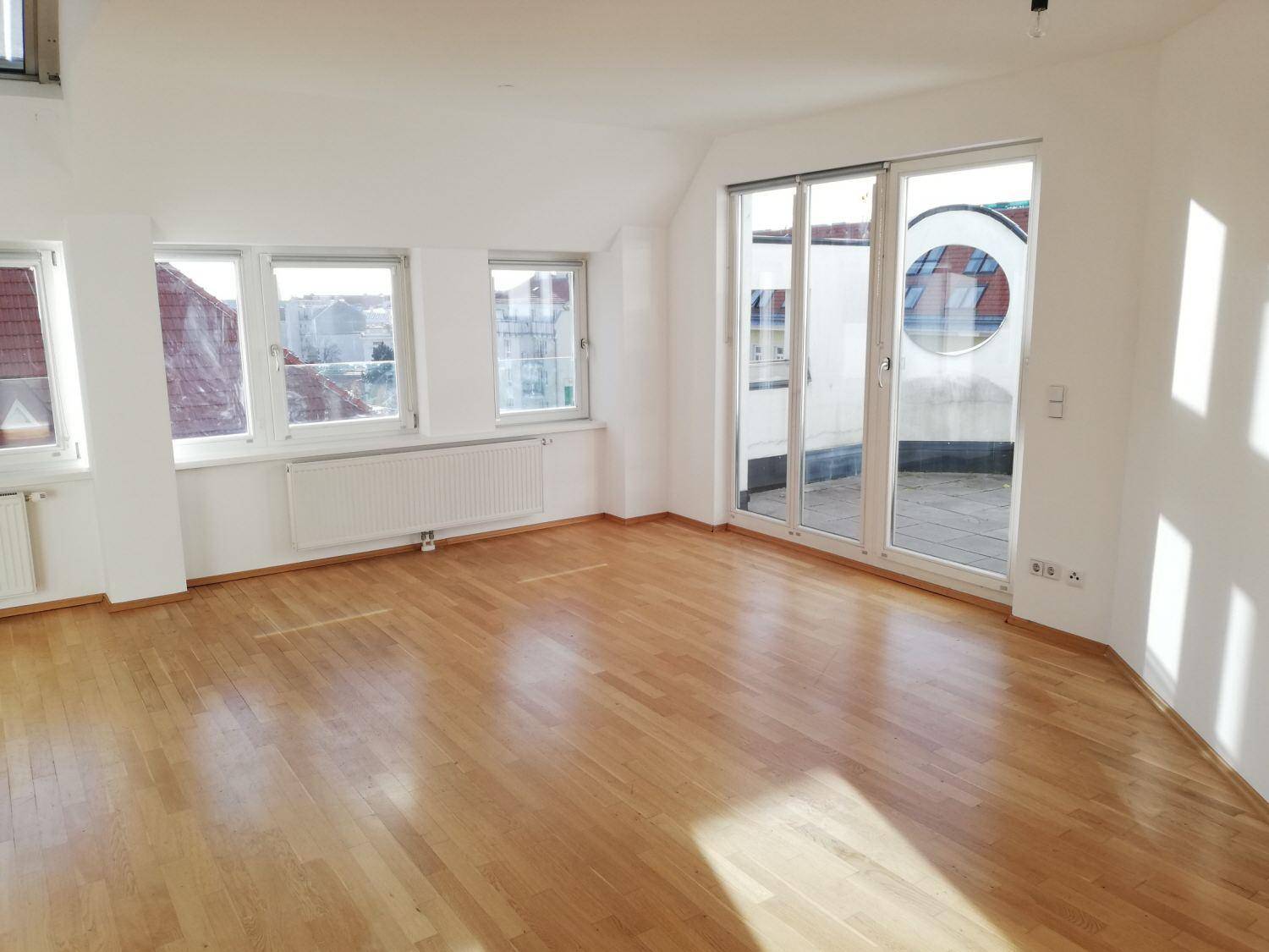 Geräumiger, heller Wohnraum mit Holzboden, mehreren Fenstern und direktem Zugang zur Terrasse.