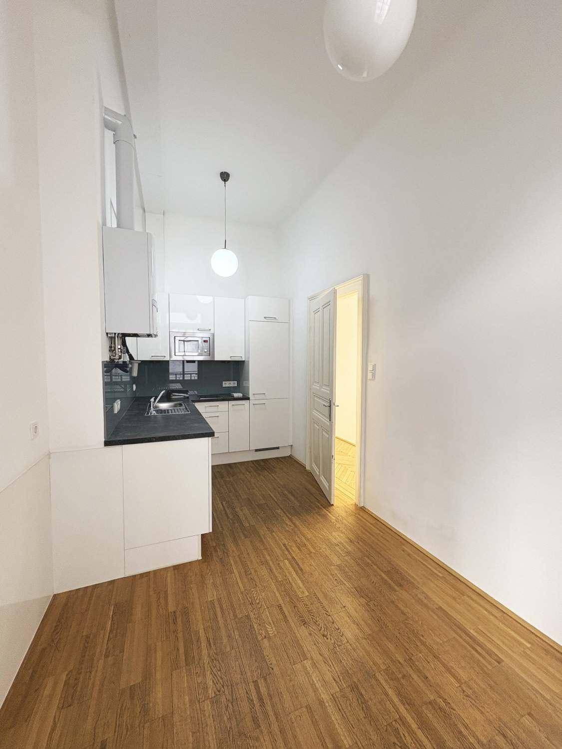 Kleine, moderne Küche mit weißen Schränken, dunkler Arbeitsplatte und Holzboden.