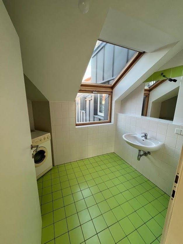 Badezimmer im Dachgeschoss mit grünen Fliesen, Waschbecken, Waschmaschine und Dachfenster.
