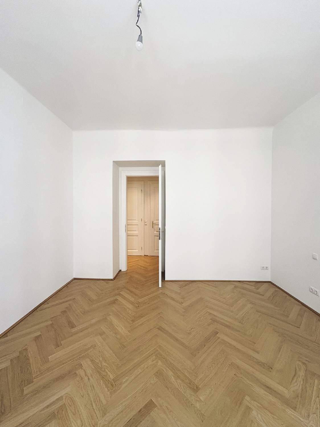 Geräumiges Zimmer mit klassischem Fischgrätparkett und weiß gestrichenen Wänden, bereit zum Einzug.