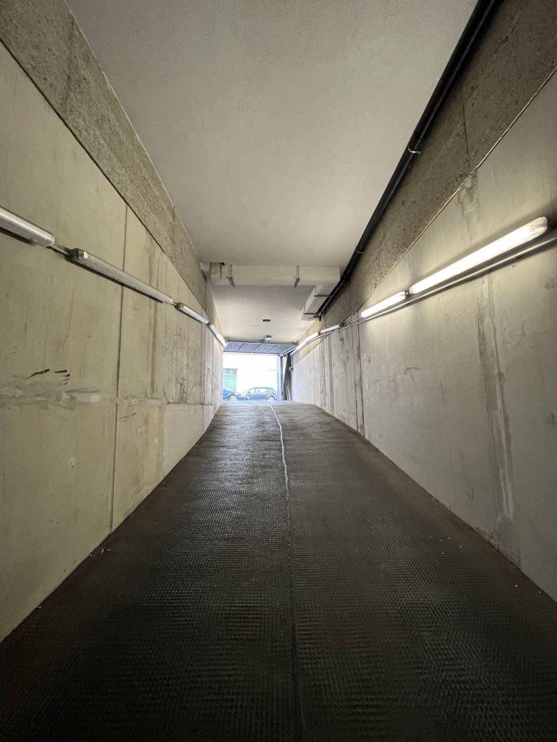 Einfahrt oder Ausfahrt einer Tiefgarage mit schrägen Betonwänden und Reihen von Leuchtstofflampen.