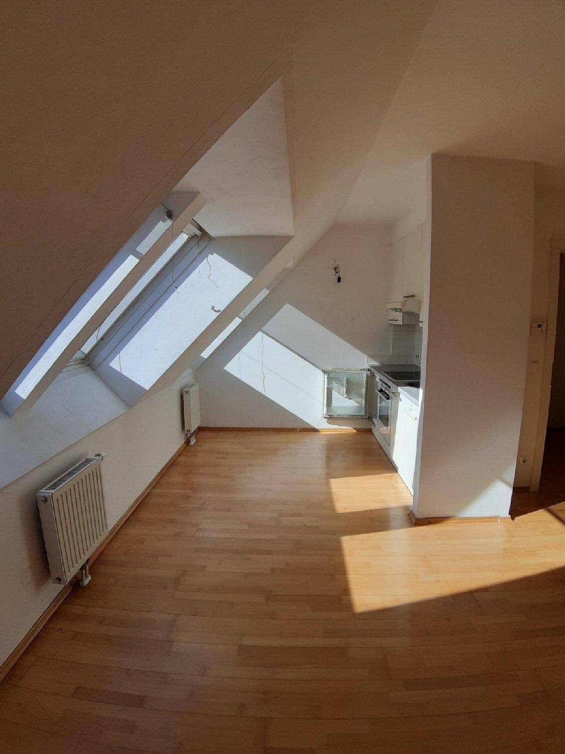 Weitläufiger Blick auf die helle Dachgeschosswohnung mit Küchenzeile, Holzboden und Dachfenstern.