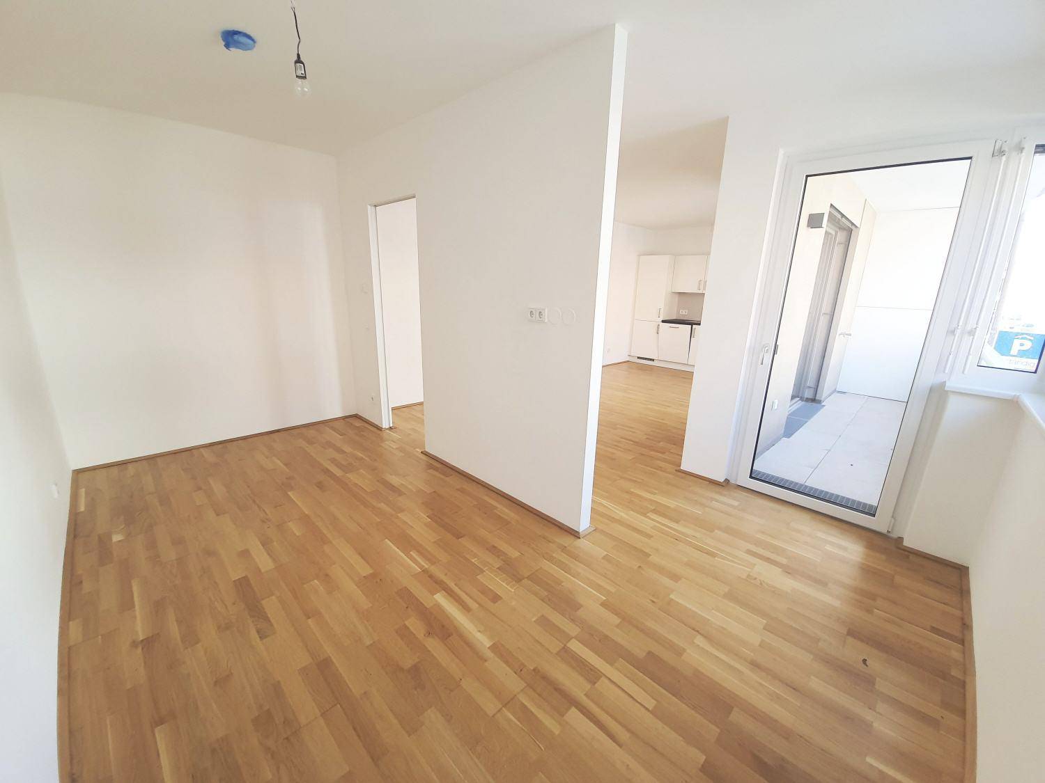 Offener Wohnbereich mit Parkettboden, der zur Küchenzeile und dem Balkon führt.