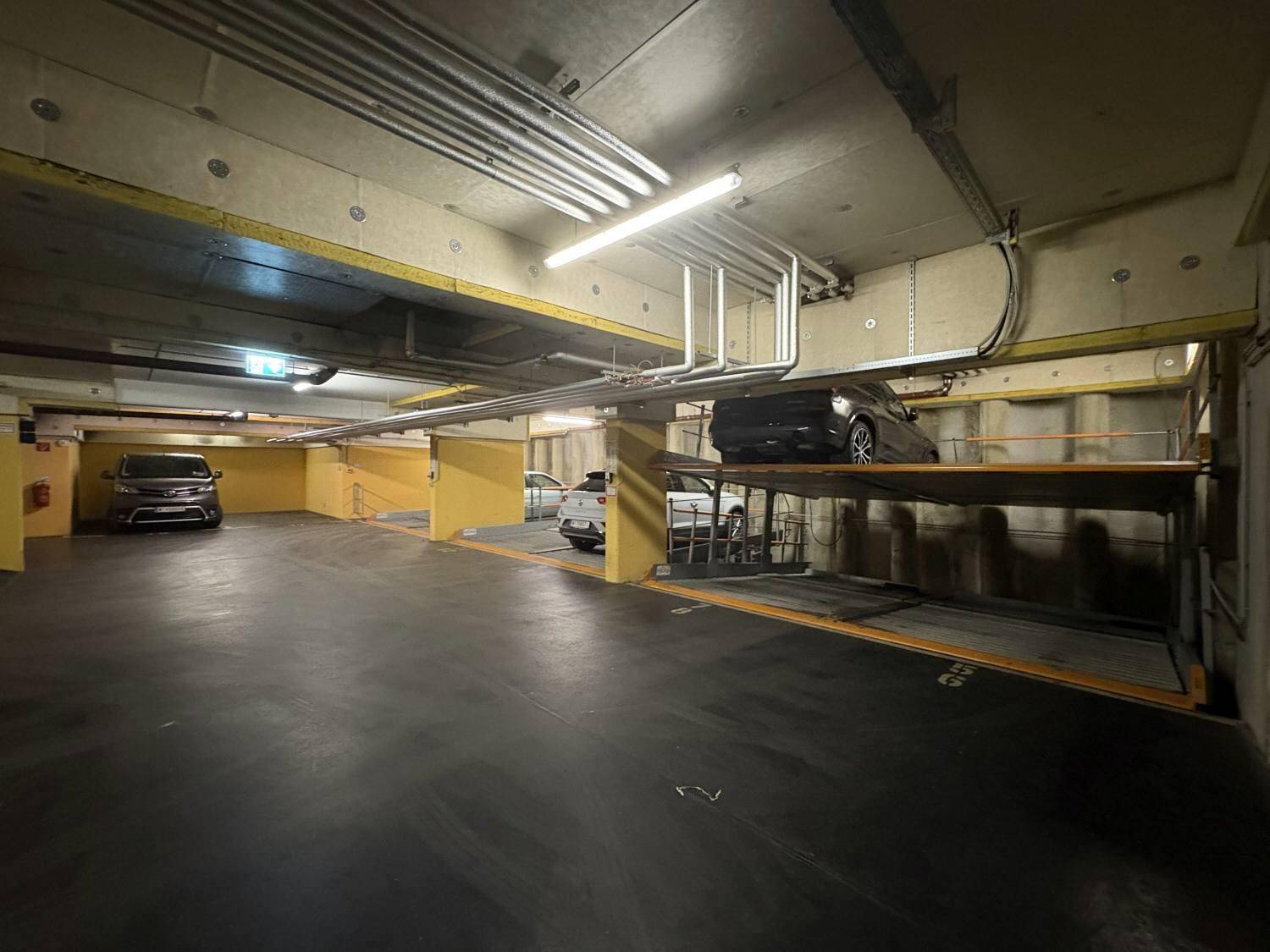 Weitläufige Tiefgarage mit mehreren Parkplätzen und doppelstöckigen Autohebebühnen.