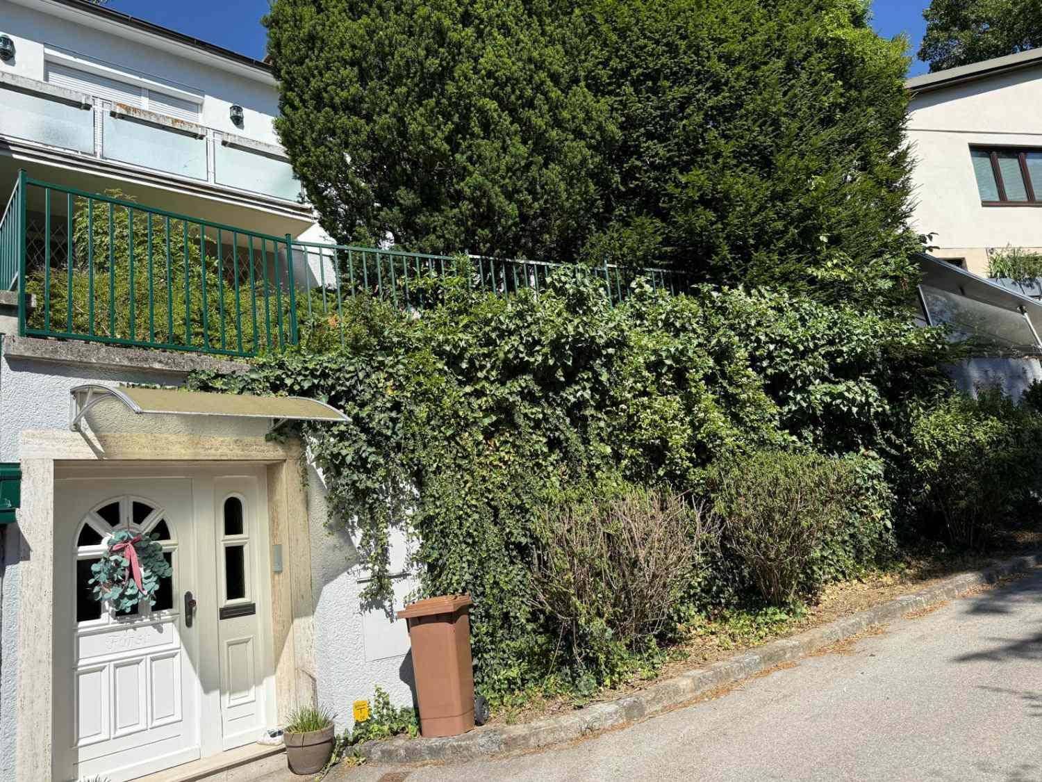 Eingangsbereich des Hauses von der Straße aus gesehen, umgeben von viel Grün.