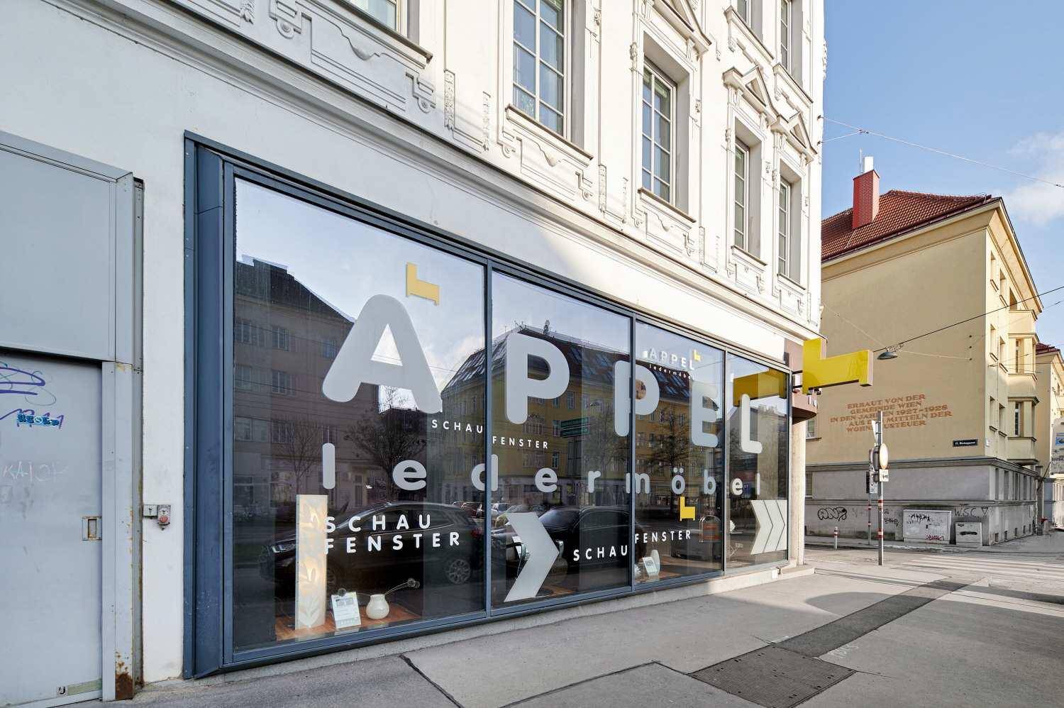 Nahaufnahme der Ladenfassade im Erdgeschoss mit großen Schaufenstern und Geschäftsreklame.
