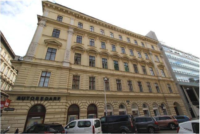 Lange Fassade eines historischen Gebäudes mit vielen Fenstern und Geschäften im Erdgeschoss.