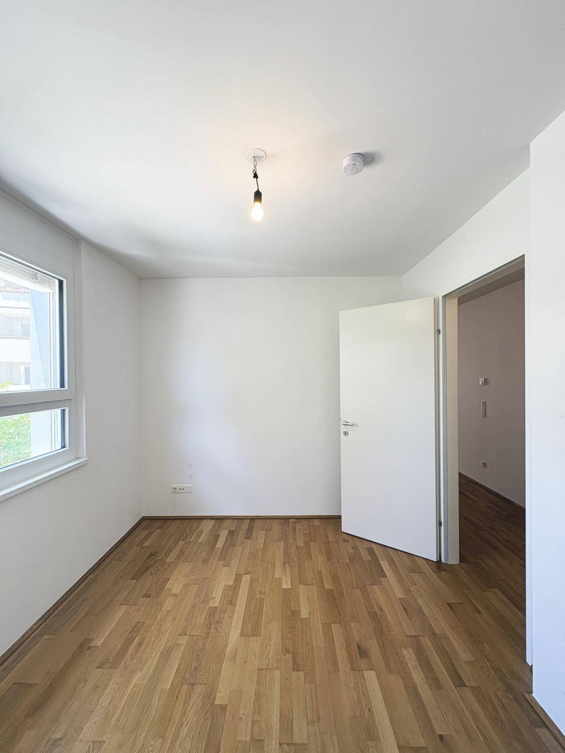 Freundliches Zimmer mit Parkettboden und Fenster, bietet vielseitige Nutzungsmöglichkeiten.