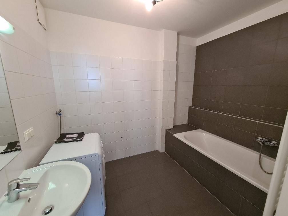 Badezimmer mit Badewanne, Waschbecken und Waschmaschine, teilweise gefliest in Weiß und Grau.
