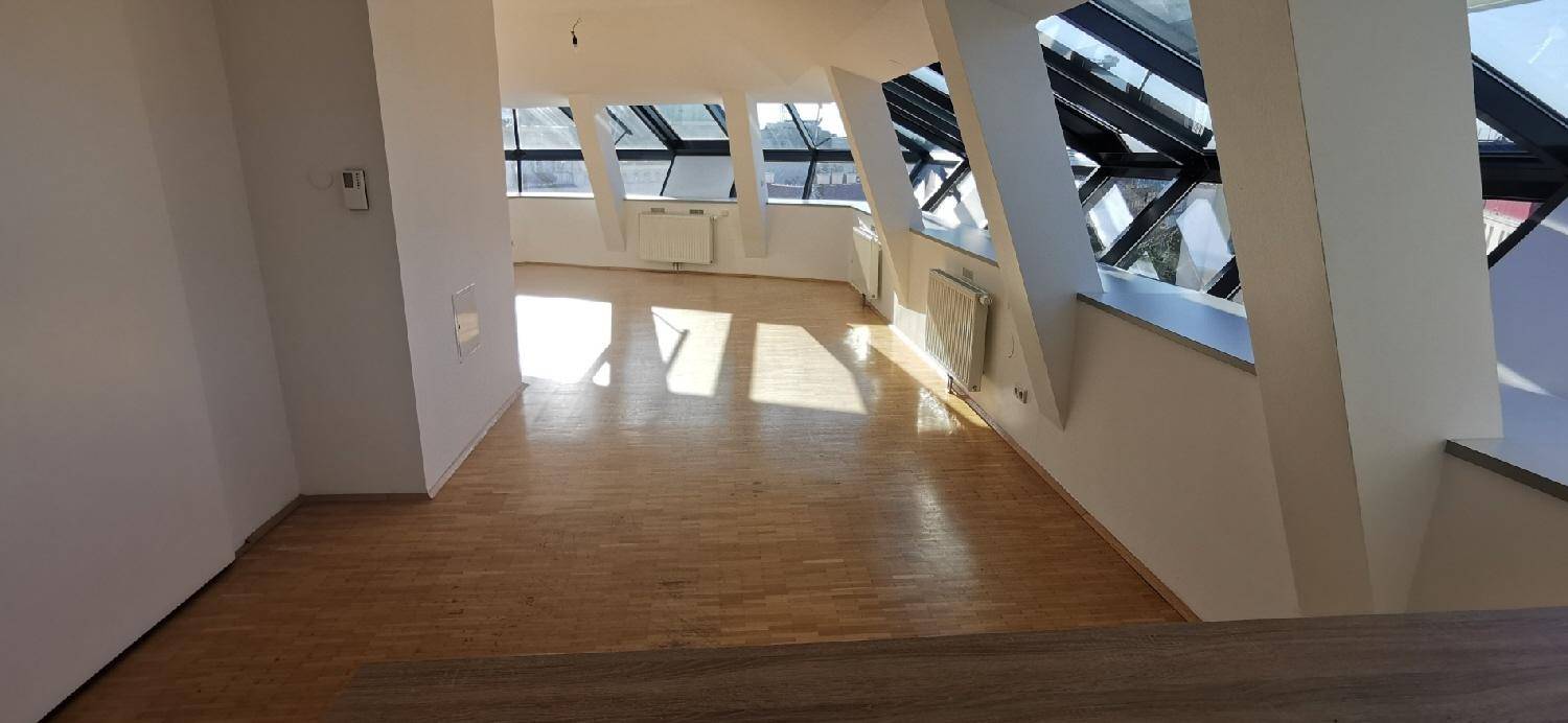 Geräumiger Wohnbereich mit Holzparkett und großen Dachfenstern, bietet viel Tageslicht und Stadtblick.
