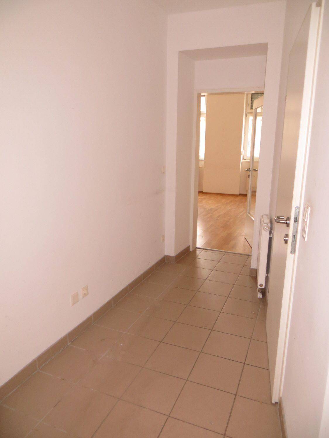 Heller Flur mit Fliesenboden, der zu einem Zimmer mit Parkett führt.