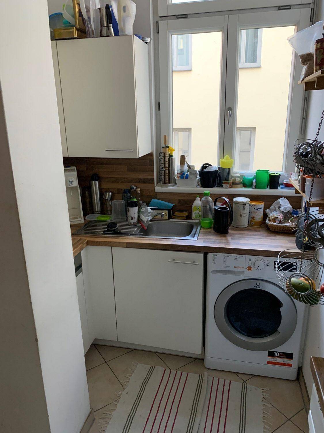 Funktionale Küche mit Spüle, Waschmaschine und Fenster für natürliches Licht und Belüftung.