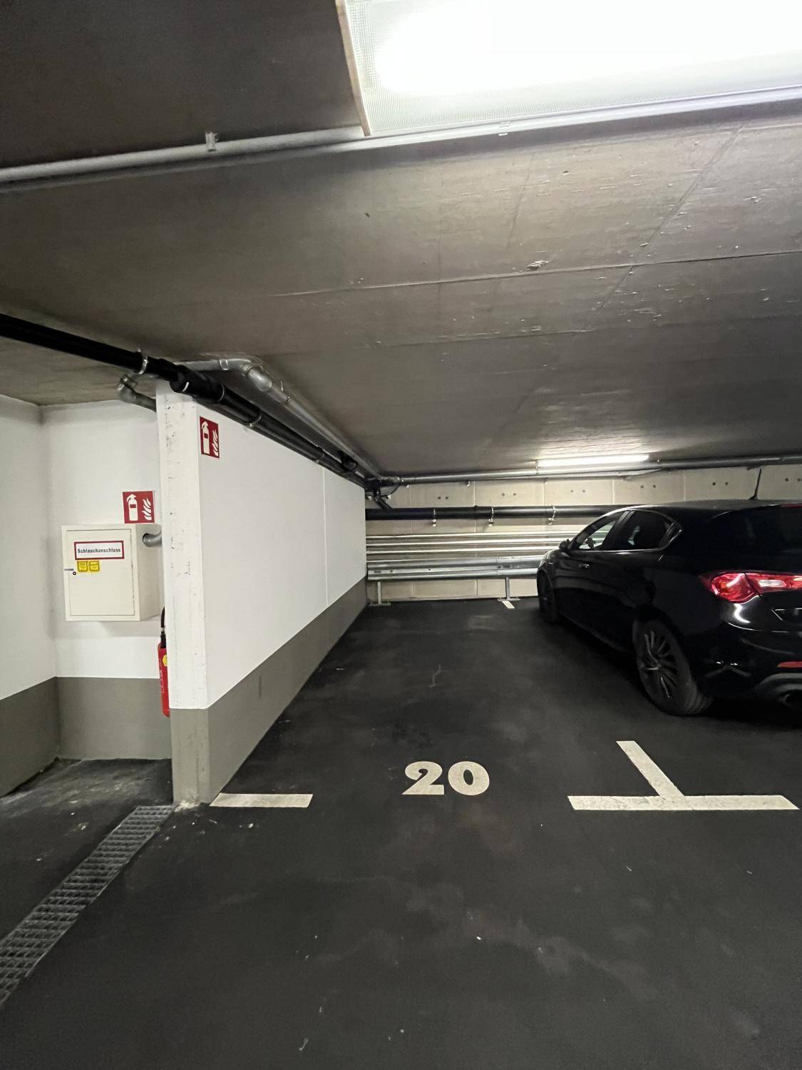 Tiefgaragenstellplatz Nummer 20 mit einem schwarzen Auto und Brandschutzvorrichtungen an der Wand.