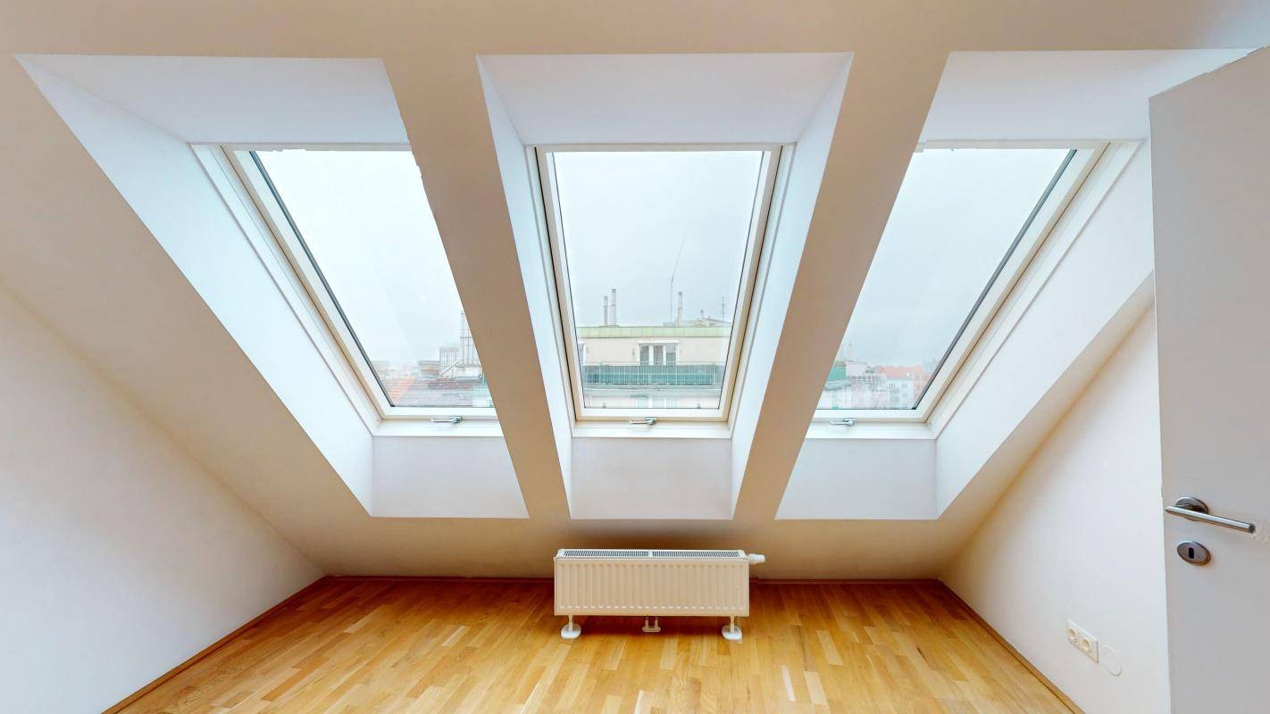 Heller Dachgeschossraum mit Holzboden und drei großen Dachfenstern, viel Tageslicht.