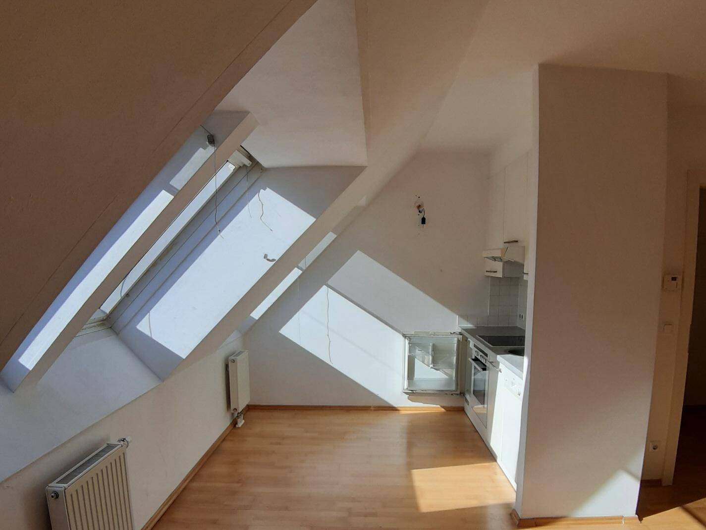 Helle Küchenzeile in einem Dachgeschossraum mit Dachfenstern, Heizkörper und Holzboden.