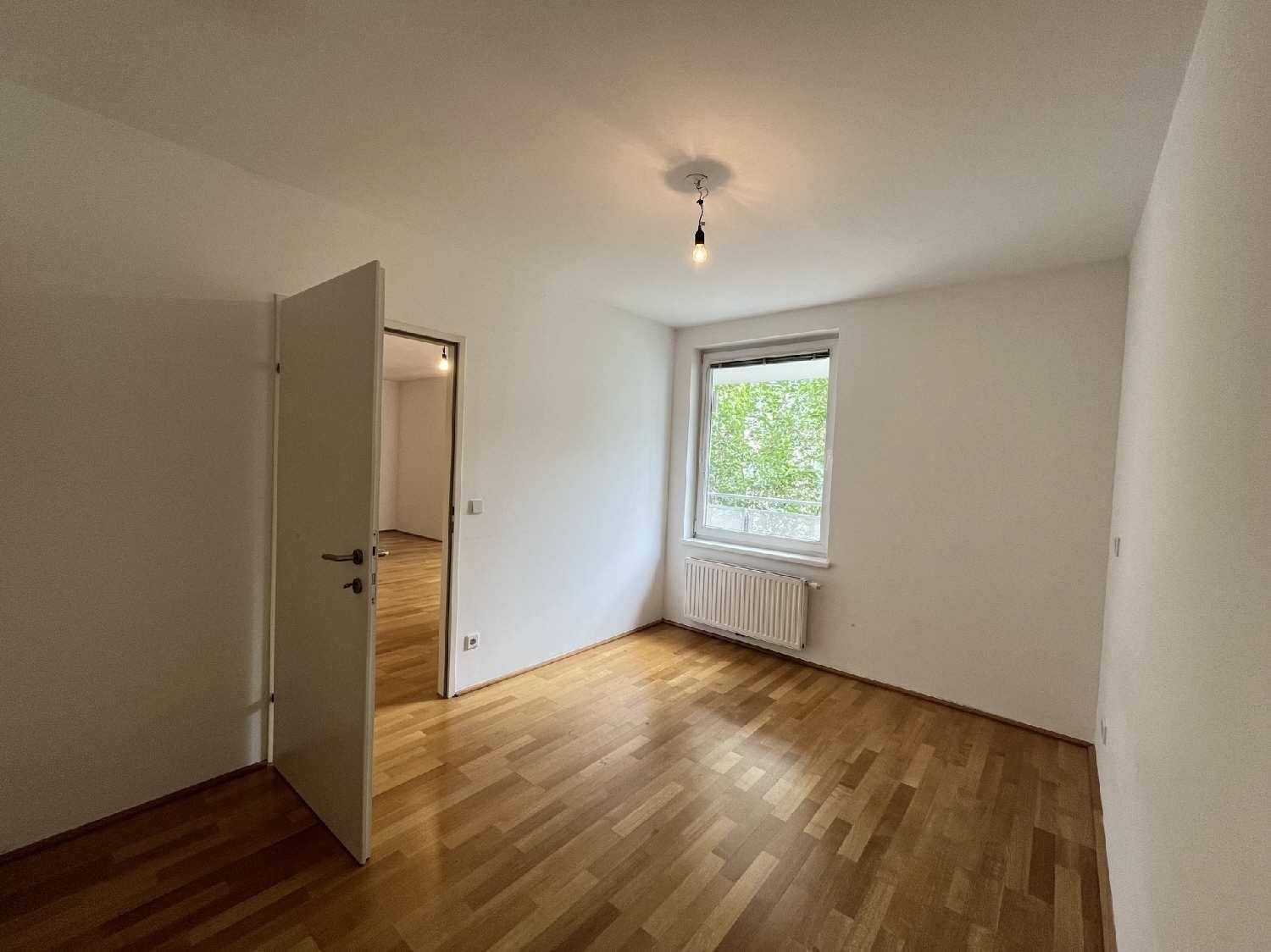 Helles Schlafzimmer mit Parkettboden und Fenster, das viel Tageslicht hereinlässt.