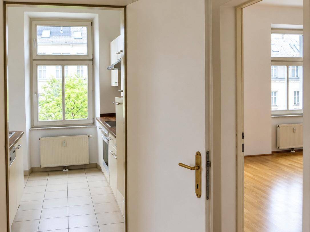Flur mit Blick in eine helle Küche und ein weiteres Zimmer, beide mit Fenstern.