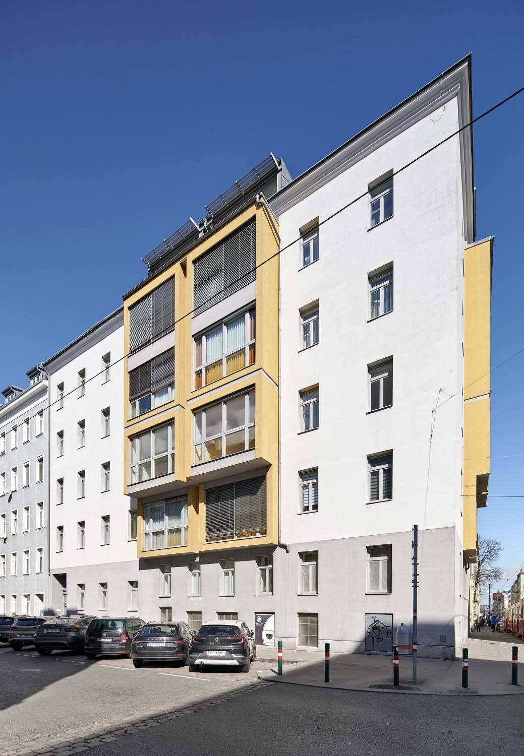 Seitenansicht des modernen Gebäudes mit gelben Akzenten und parkenden Autos auf der Straße.