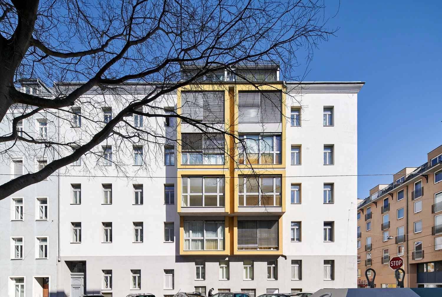 Moderne Gebäudefassade mit gelben Akzenten und vielen Fenstern in städtischer Umgebung.