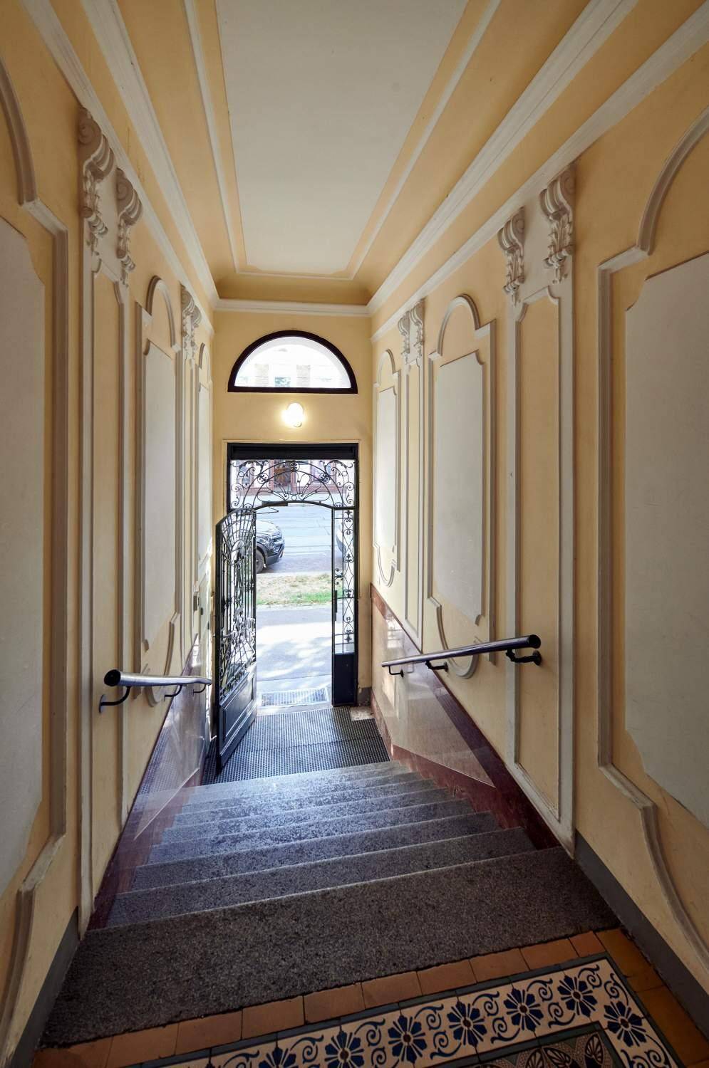 Historischer Eingangsbereich mit Treppe, Stuckelementen und schmiedeeisernem Tor.