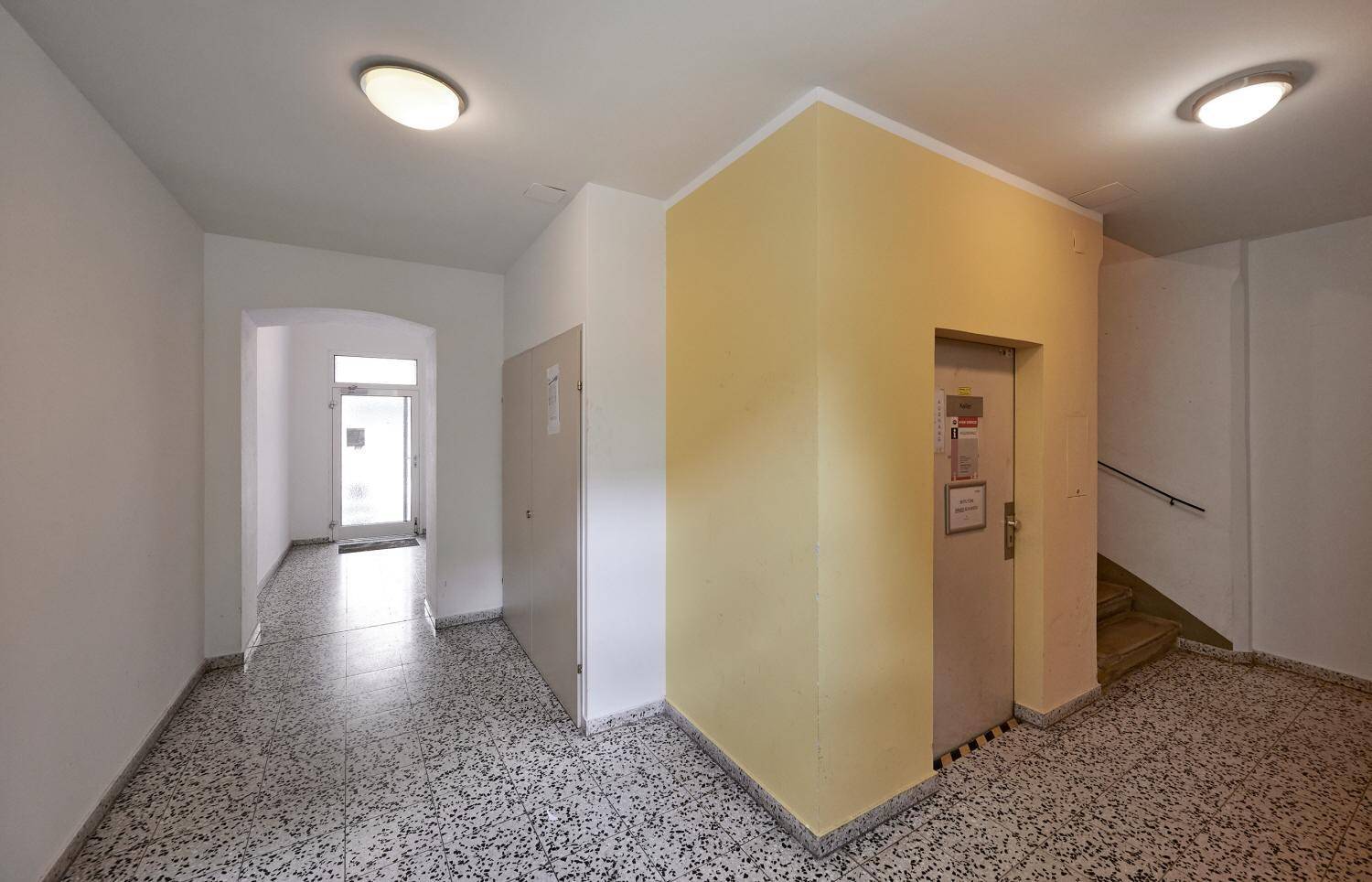Gemeinschaftsflur mit Fliesenboden, Aufzug und Treppenhauszugang in einem Mehrfamilienhaus.
