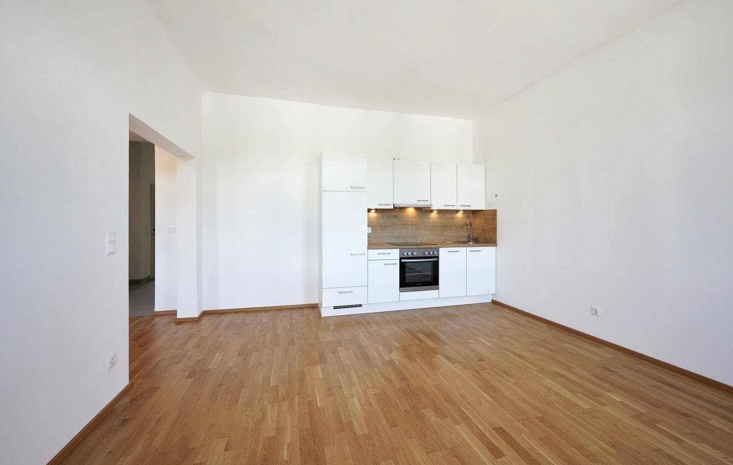 Heller Raum mit Parkettboden und einer modernen, weißen Küchenzeile an der Wand.