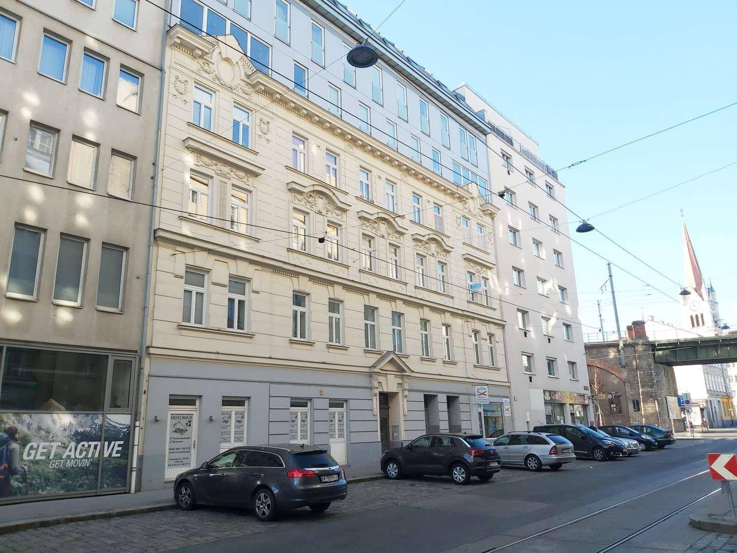 Historisches Gebäude mit klassischer Fassade und modernen Anbauten in einer städtischen Umgebung.
