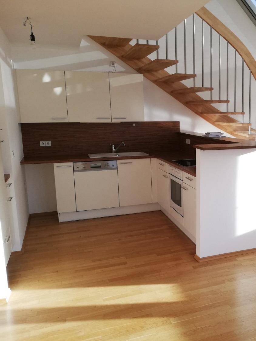 Moderne Einbauküche mit weißen Schränken, Holzarbeitsplatte und integrierten Geräten unter der Treppe.