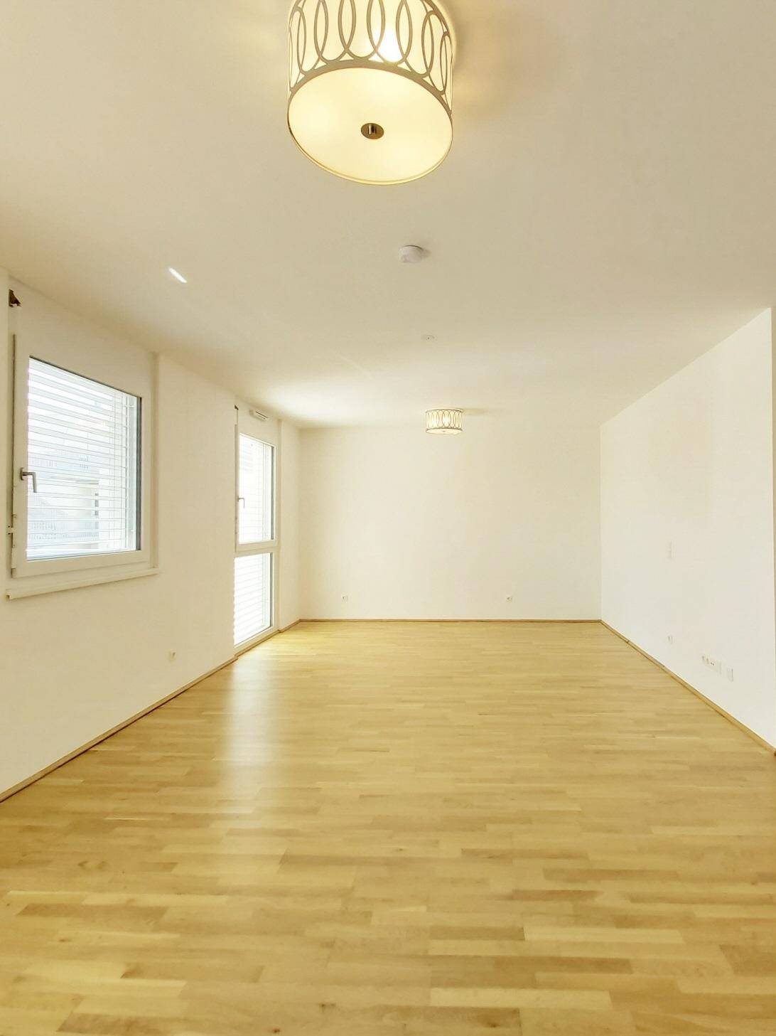 Geräumiger, heller Raum mit Parkettboden und großen Fenstern, ideal für ein Wohnzimmer.