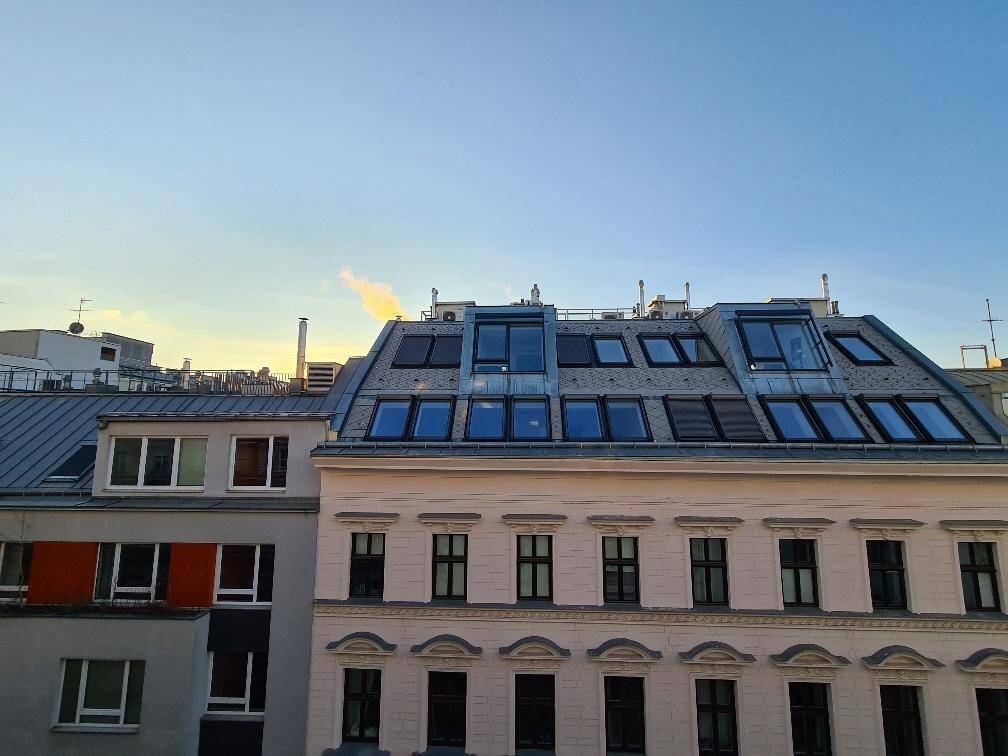 Dachlandschaft eines Gebäudes mit zahlreichen Dachfenstern und Solarpaneelen unter einem klaren Himmel.