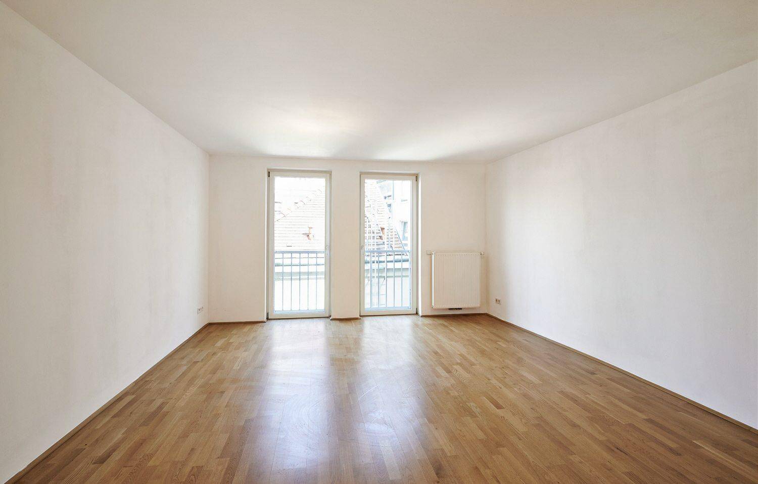 Geräumiges, helles Zimmer mit Parkettboden und zwei französischen Balkonen, die viel Licht hereinlassen.