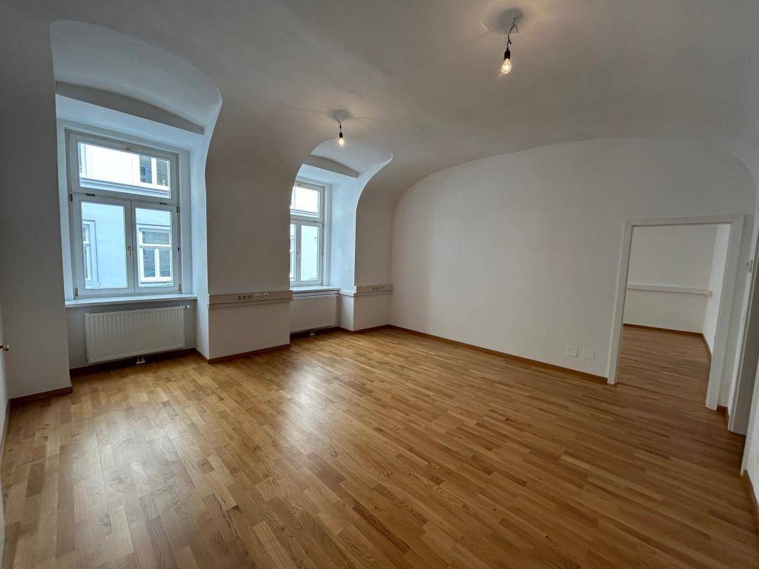 Großes Wohnzimmer mit Holzboden, hohen Fenstern und gewölbten Decken.