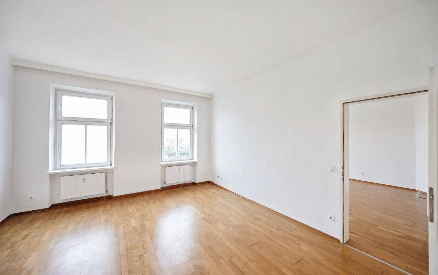 Geräumiges Zimmer mit klassischem Parkettboden und einem offenen Durchgang zu einem weiteren Raum.
