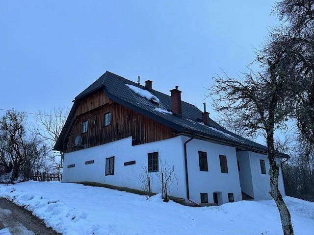 Seitenansicht eines gepflegten weißen Hauses mit Holzbalkon und dunklem Dach im Schnee.