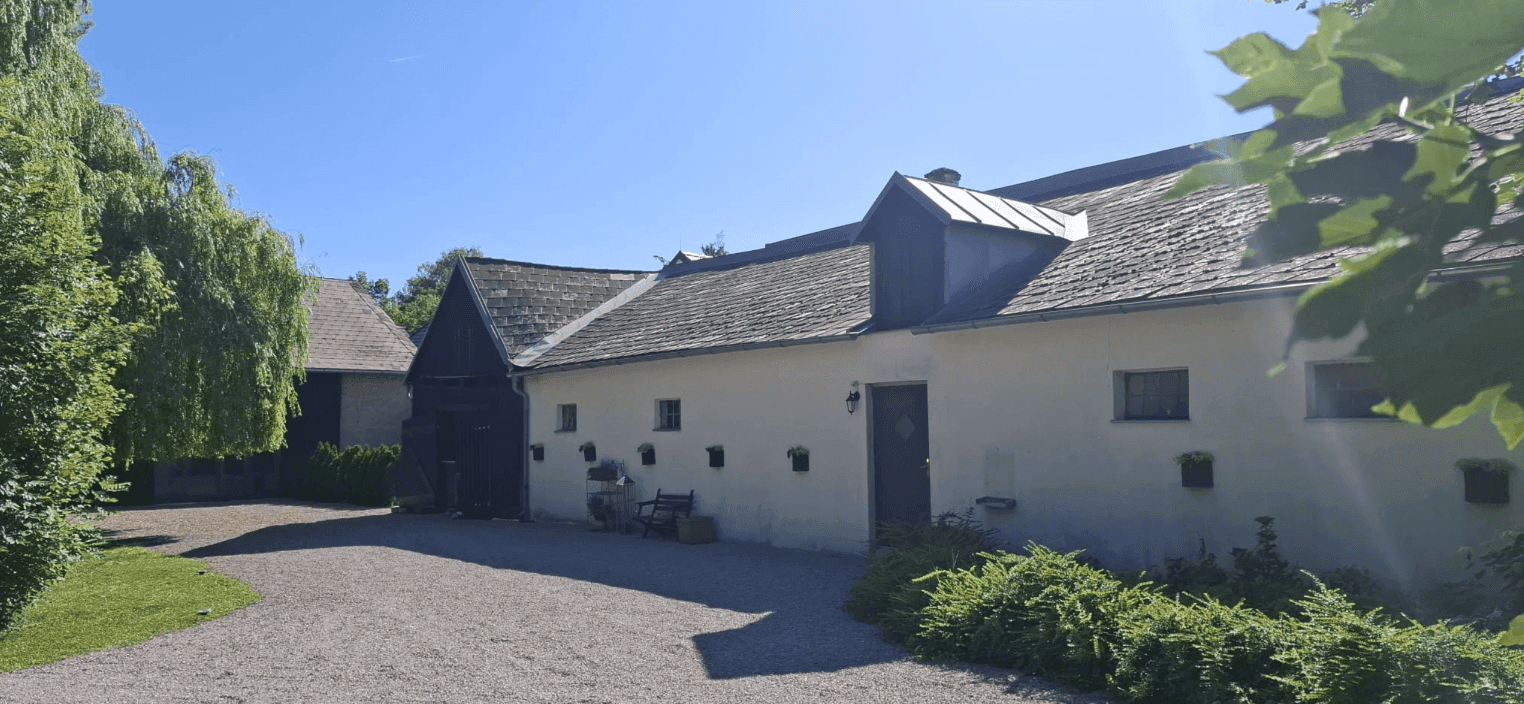 Die Fassade eines traditionellen Gebäudes mit weiß getünchten Wänden und dunklen Holzelementen, umgeben von einem Kiesbereich.