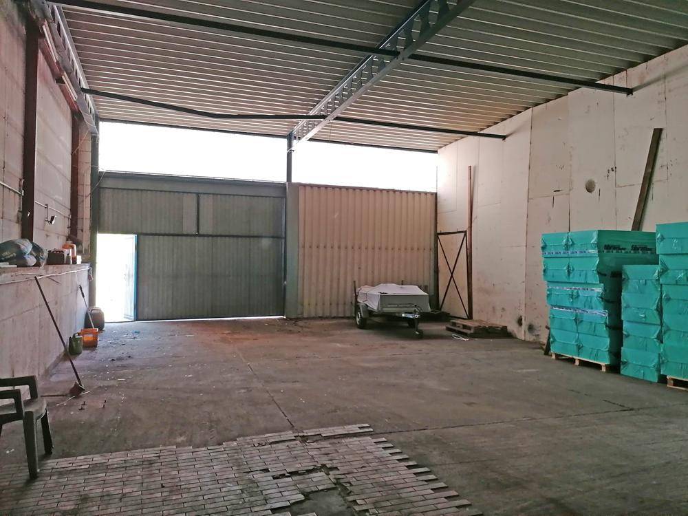 Große Lagerhalle mit offenem Tor, Betonboden und sichtbaren Deckenstrukturen, bereit zur Nutzung.