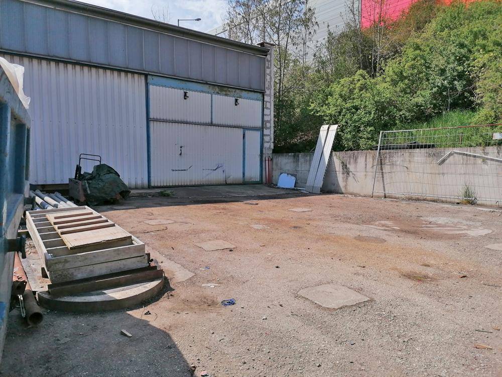 Außenansicht der Lagerhalle mit Metallfassade, großem Vorplatz und angrenzendem Grünbereich.