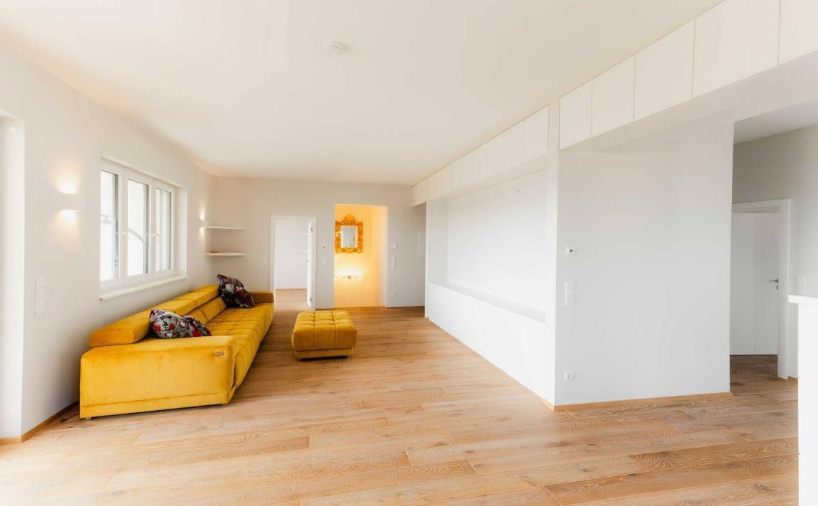 Helles Wohnzimmer mit modernem gelben Sofa, Holzboden und indirekter Beleuchtung.