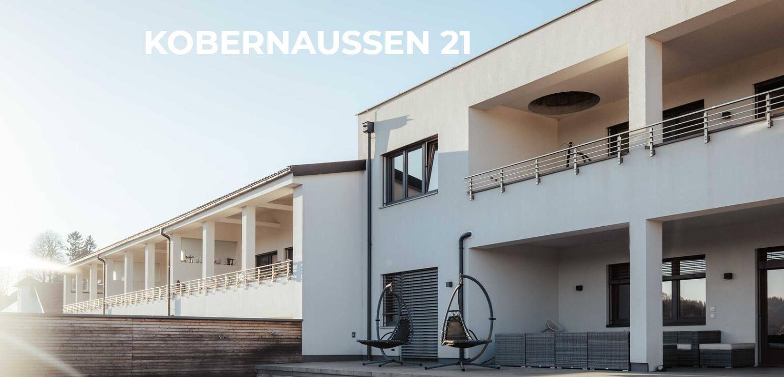 Moderne Architektur des Gebäudes mit mehreren Balkonen und einer sonnigen Terrasse im Vordergrund.