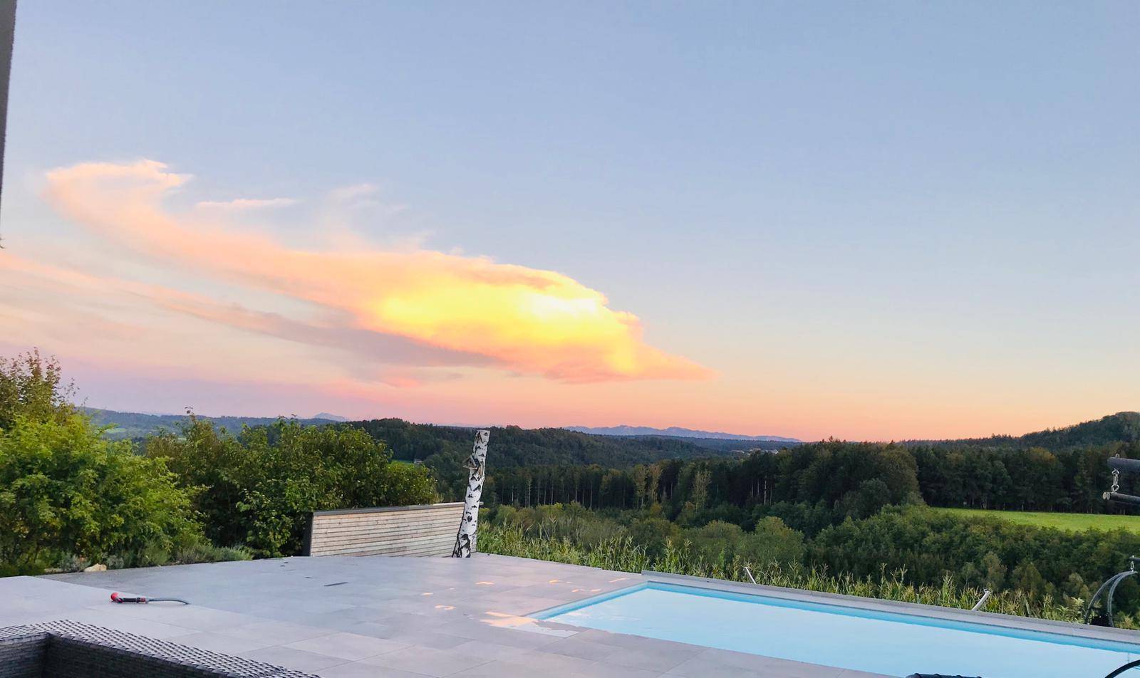 Außenpool mit atemberaubendem Blick auf die grüne Landschaft bei Sonnenuntergang.
