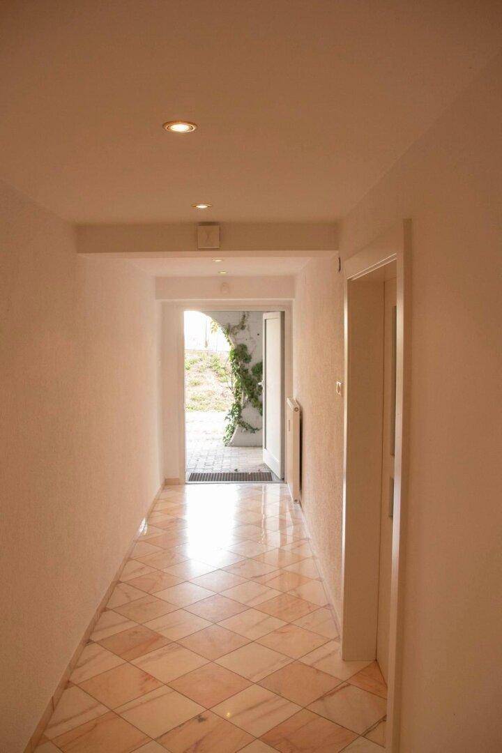 Heller Flur mit gemusterten Fliesen und Blick durch die offene Tür ins Grüne.