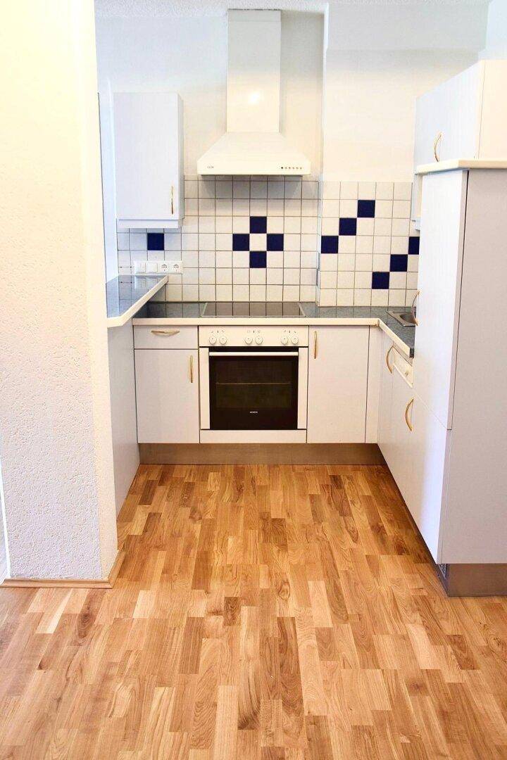 Kompakte Einbauküche mit weißen Schränken, Herd und Dunstabzugshaube auf Holzboden.