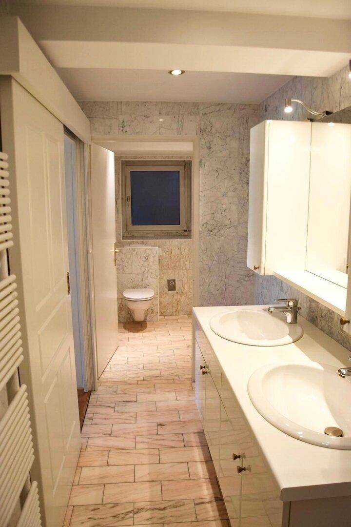 Modernes Badezimmer mit Doppelwaschbecken, Spiegelschrank und separatem WC-Bereich.