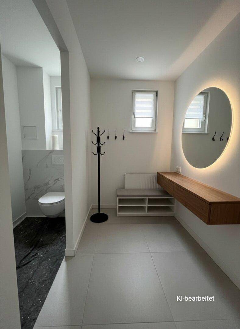 Heller Flur mit modernem Spiegel, Holzkonsole und Zugang zu einem separaten WC.
