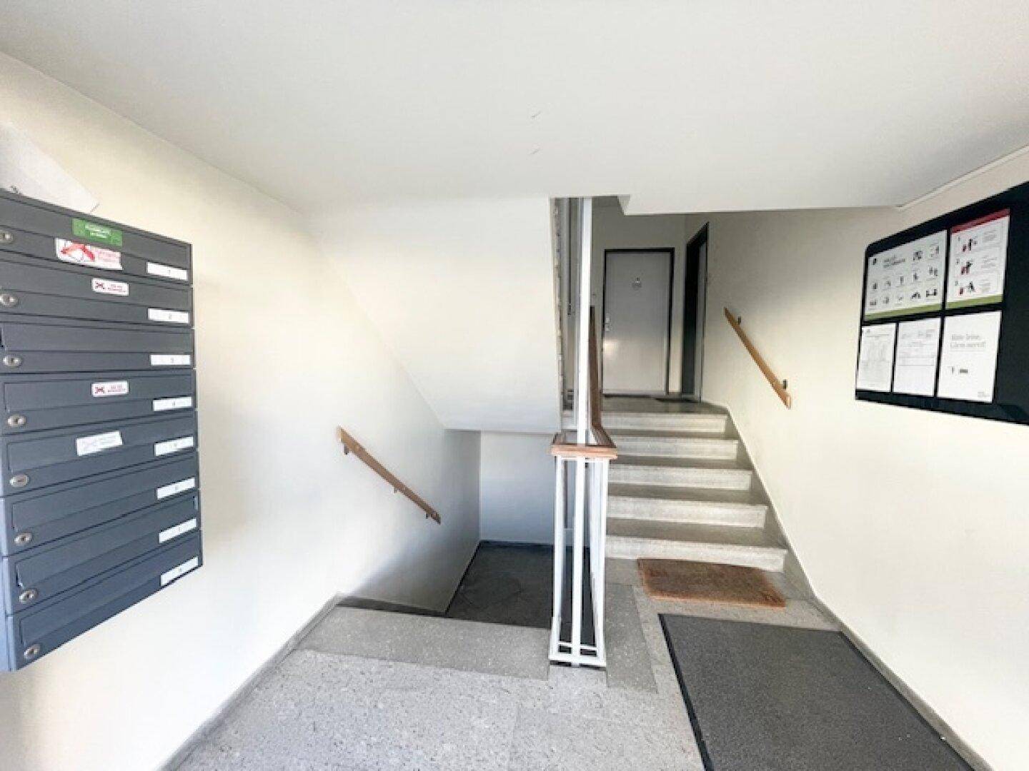 Heller Eingangsbereich mit Treppenhaus, Briefkästen und Informationsaushängen.