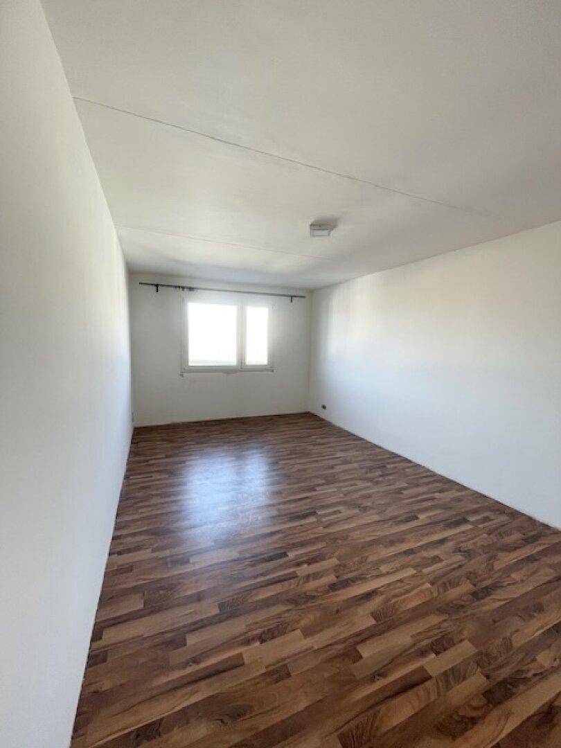 Leeres Zimmer mit Laminatboden und einem Fenster, das viel Tageslicht hereinlässt.