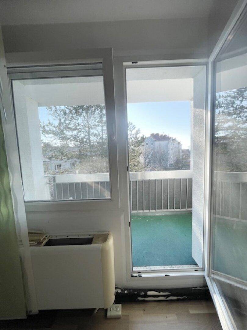 Blick von innen auf einen kleinen Balkon mit Geländer und Aussicht auf die Umgebung.