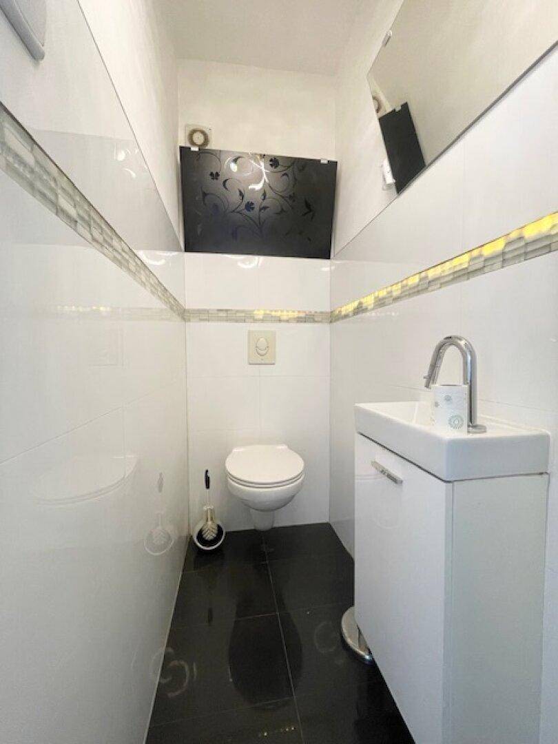 Modernes Gäste-WC mit wandhängender Toilette, kleinem Waschbecken und dunklen Bodenfliesen.
