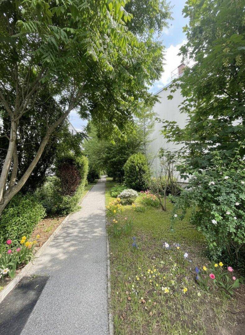 Idyllischer Gartenweg umgeben von üppigem Grün, Blumenbeeten und hohen Bäumen.
