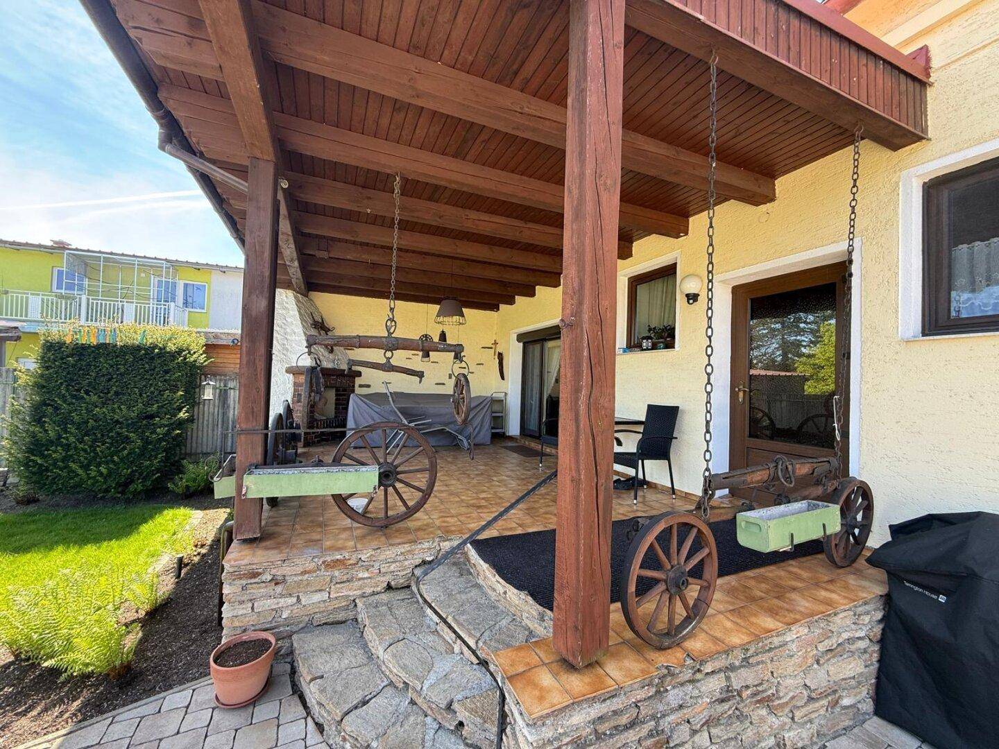 Überdachte Terrasse mit Holzbalken, rustikaler Dekoration und Zugang zum Garten.
